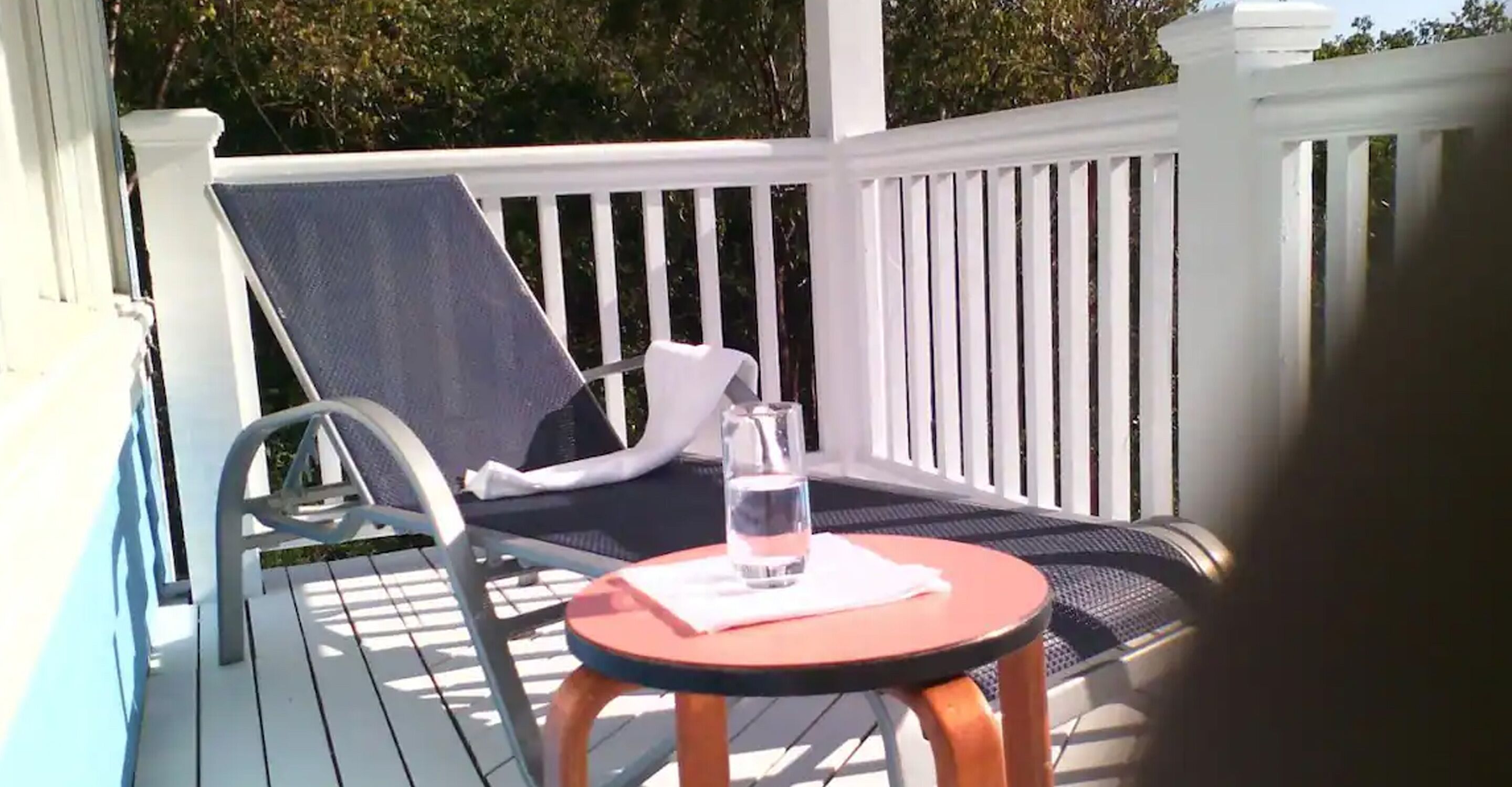 Una terraza con mesa y sillas, un vaso de agua y una barandilla blanca.