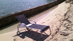 Une chaise de plage près du bord de l’eau, avec une barrière en béton et une plage de sable.