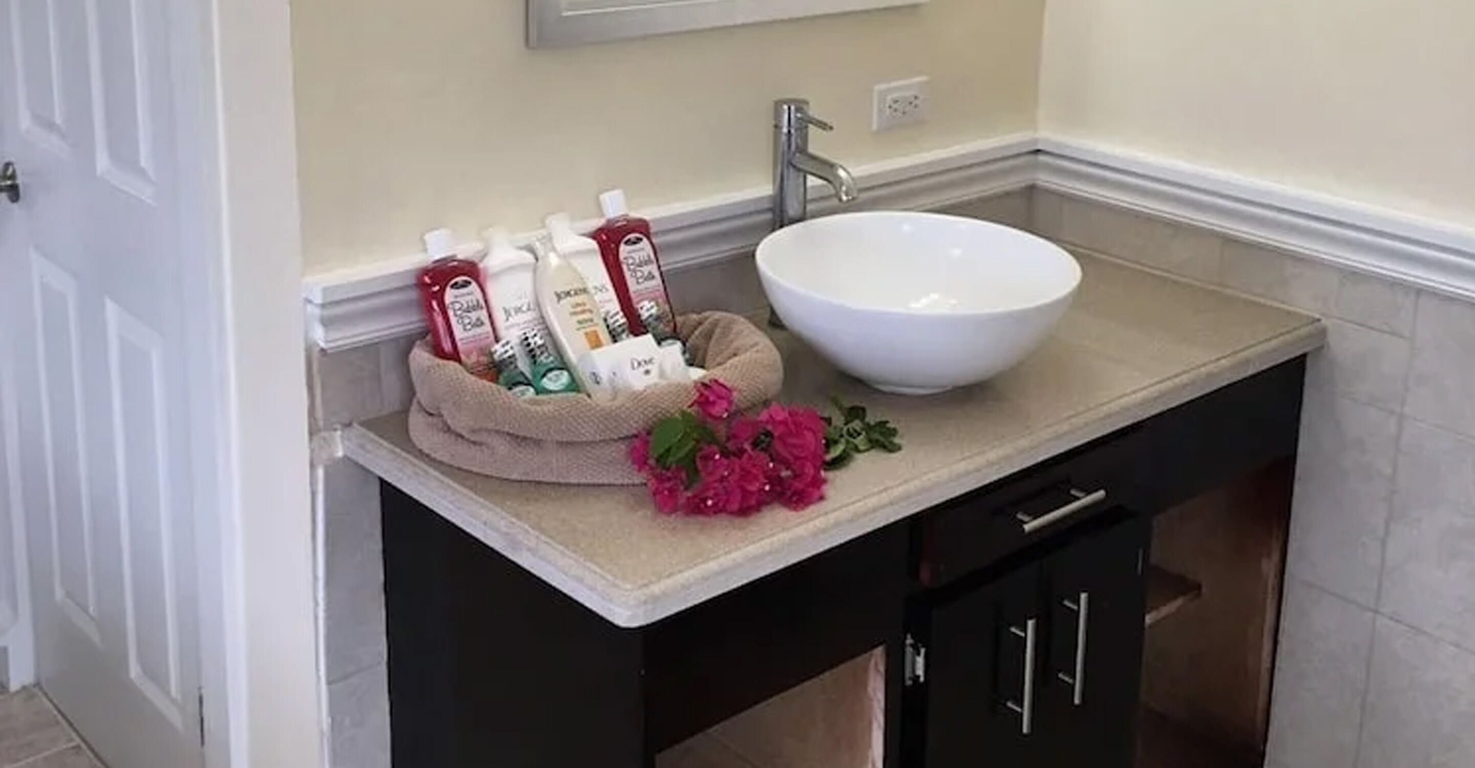 Une salle de bain avec un lavabo blanc, des meubles sombres et un porte-serviettes où sont rangés les articles de toilette.