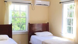 Une chambre avec deux lits simples, une fenêtre et un appareil de climatisation.