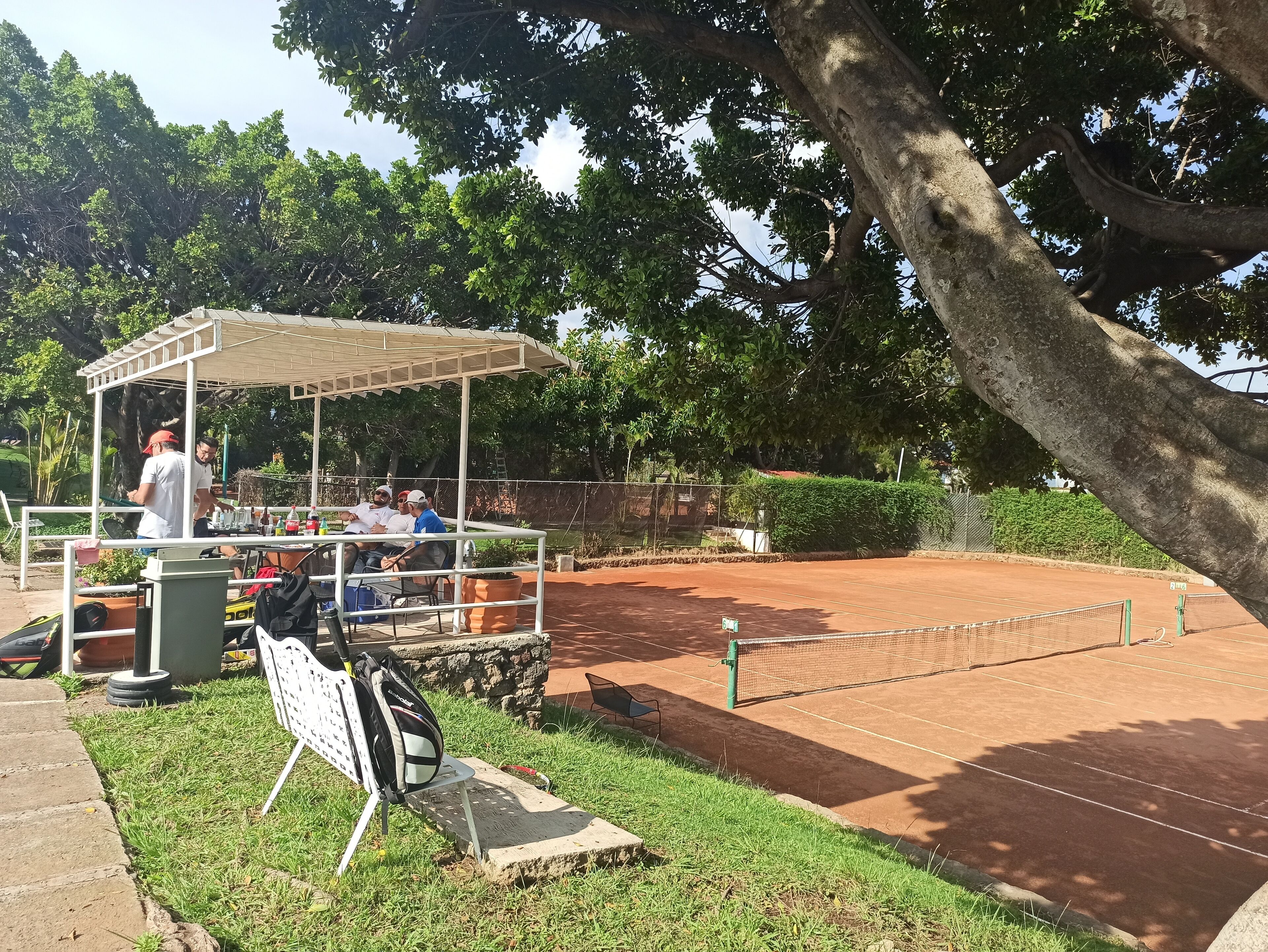 Una cancha de tenis con red, una zona de estar techada y un puesto de comida.