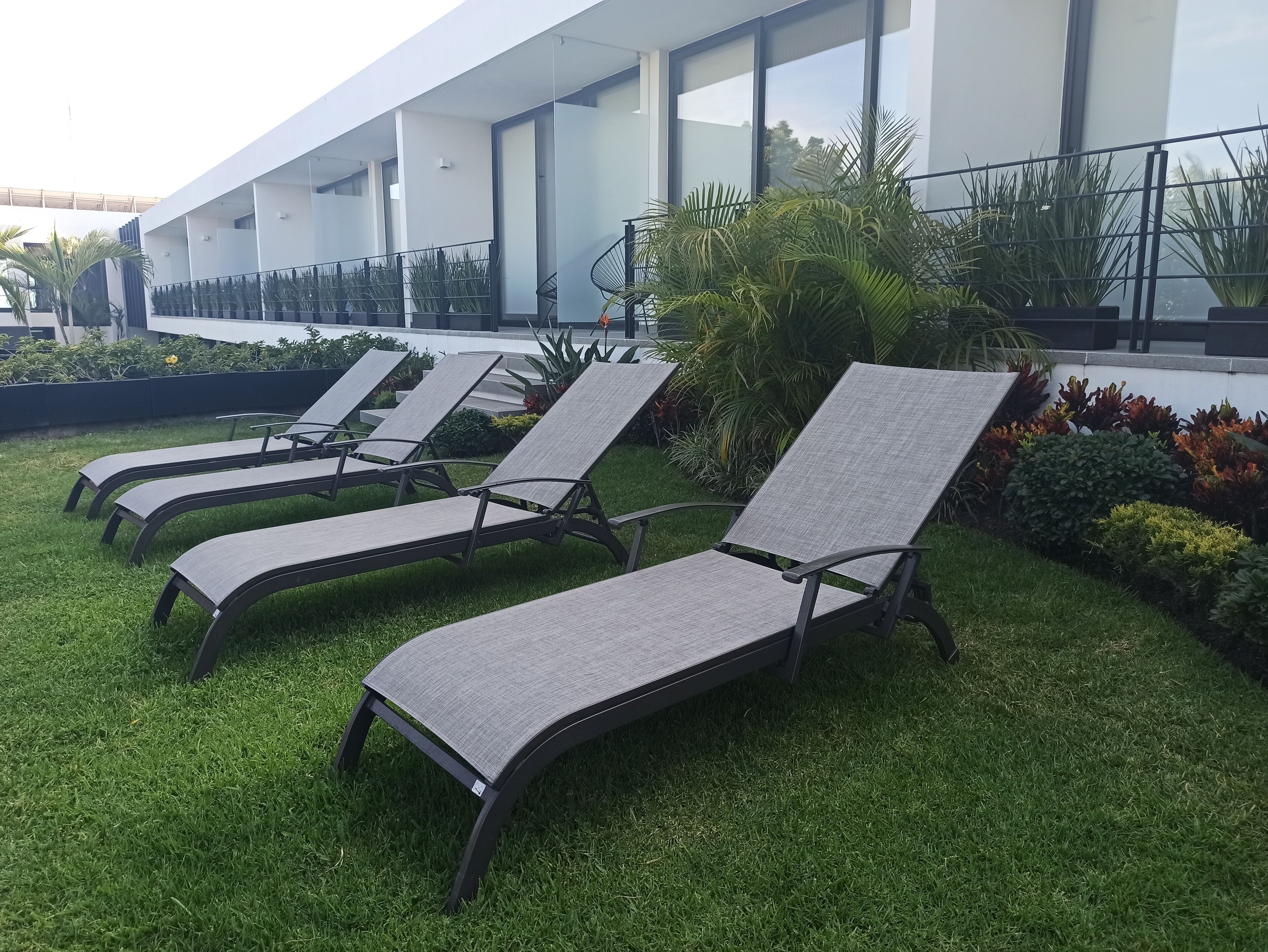 Sillas de descanso al aire libre dispuestas sobre una zona verde, con un edificio moderno al fondo.