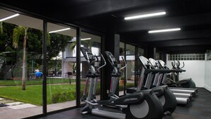 Una palestra con tapis roulant ed ellittiche, ampie finestre e vista su un parco.