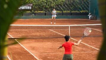 A tennis court with a net in the center, surrounded by greenery and a sign that reads "SPORTENIS".