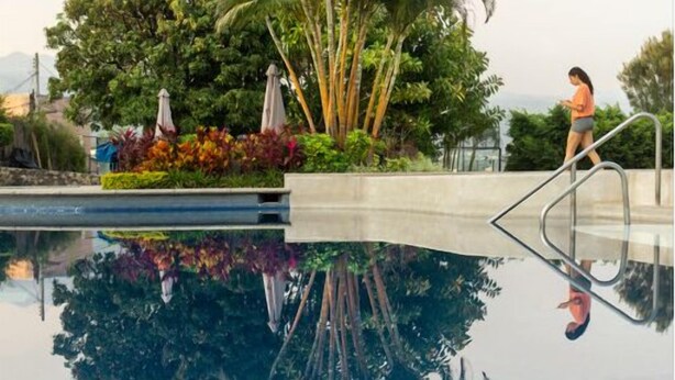 Una piscina con il riflesso limpido di palme e una persona che cammina.