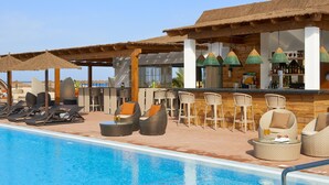 Ein Poolbereich mit Liegestühlen, einer Bar und Sonnenschirmen.