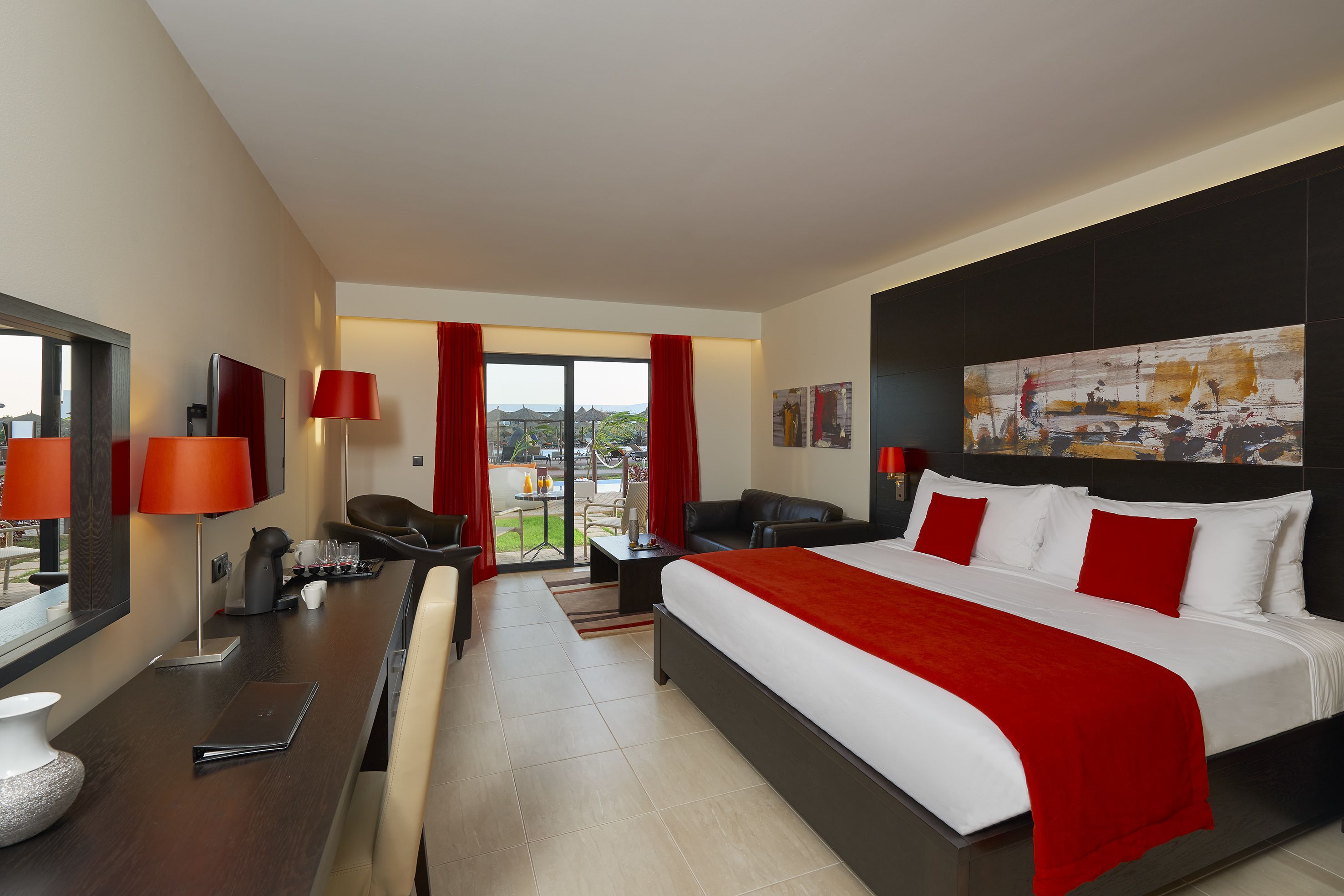 Habitación de hotel con una cama grande, un escritorio con silla, un sofá y vistas al exterior.