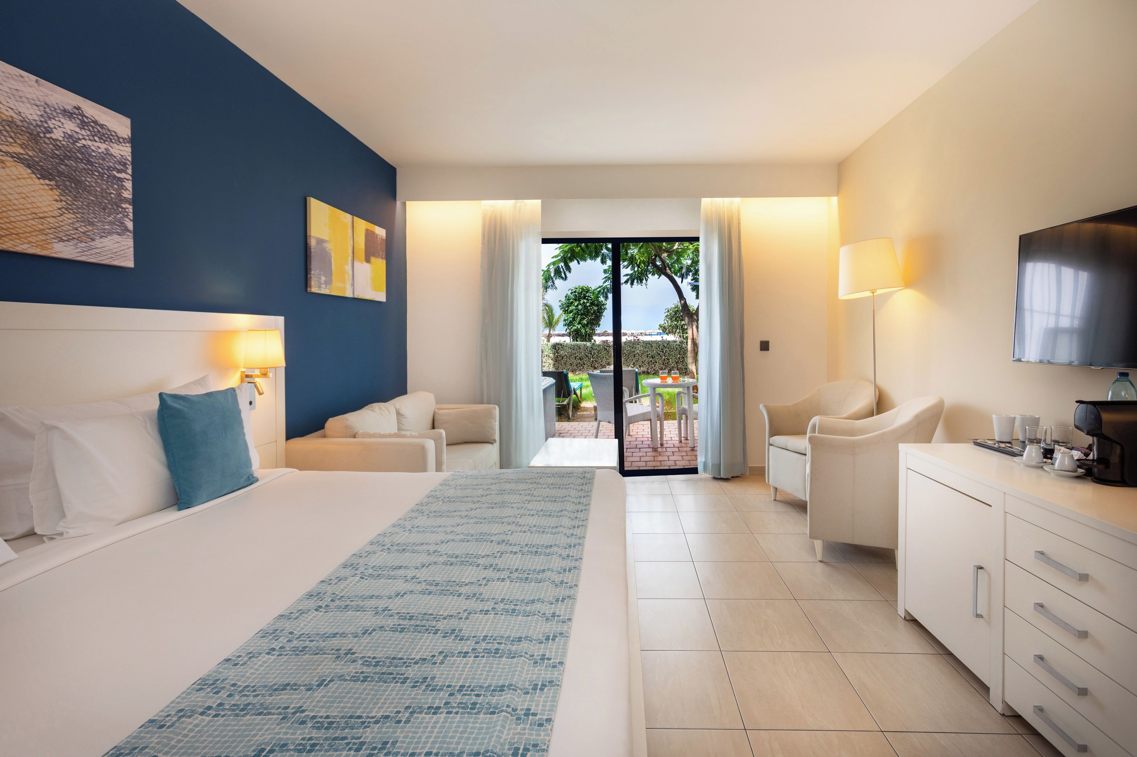 Habitación de hotel con cama, escritorio, silla, televisor y vistas al exterior.