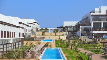 A resort with a swimming pool, outdoor seating, and a clear blue sky.