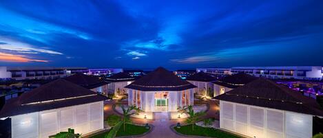 A resort with multiple thatched-roof buildings, a central open pavilion, and a well-maintained garden area.