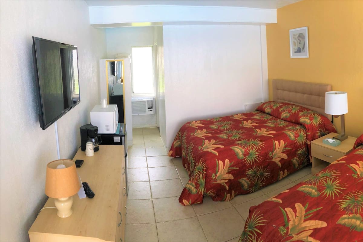 Habitación de hotel con dos camas, un escritorio con lámpara, televisión y obras de arte en las paredes.