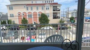 A balcony with a round table and two chairs, overlooking a street with parked cars and buildings. - Isle of Capri Motel (North Wildwood)
