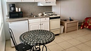 A compact kitchen with white cabinets, a microwave, a stove, and a sink. There's a small table with chairs and a TV mounted on the wall. - Isle of Capri Motel (North Wildwood)