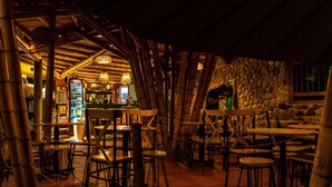Un restaurante interior con pilares de bambú, mesas de madera y una pared de piedra.