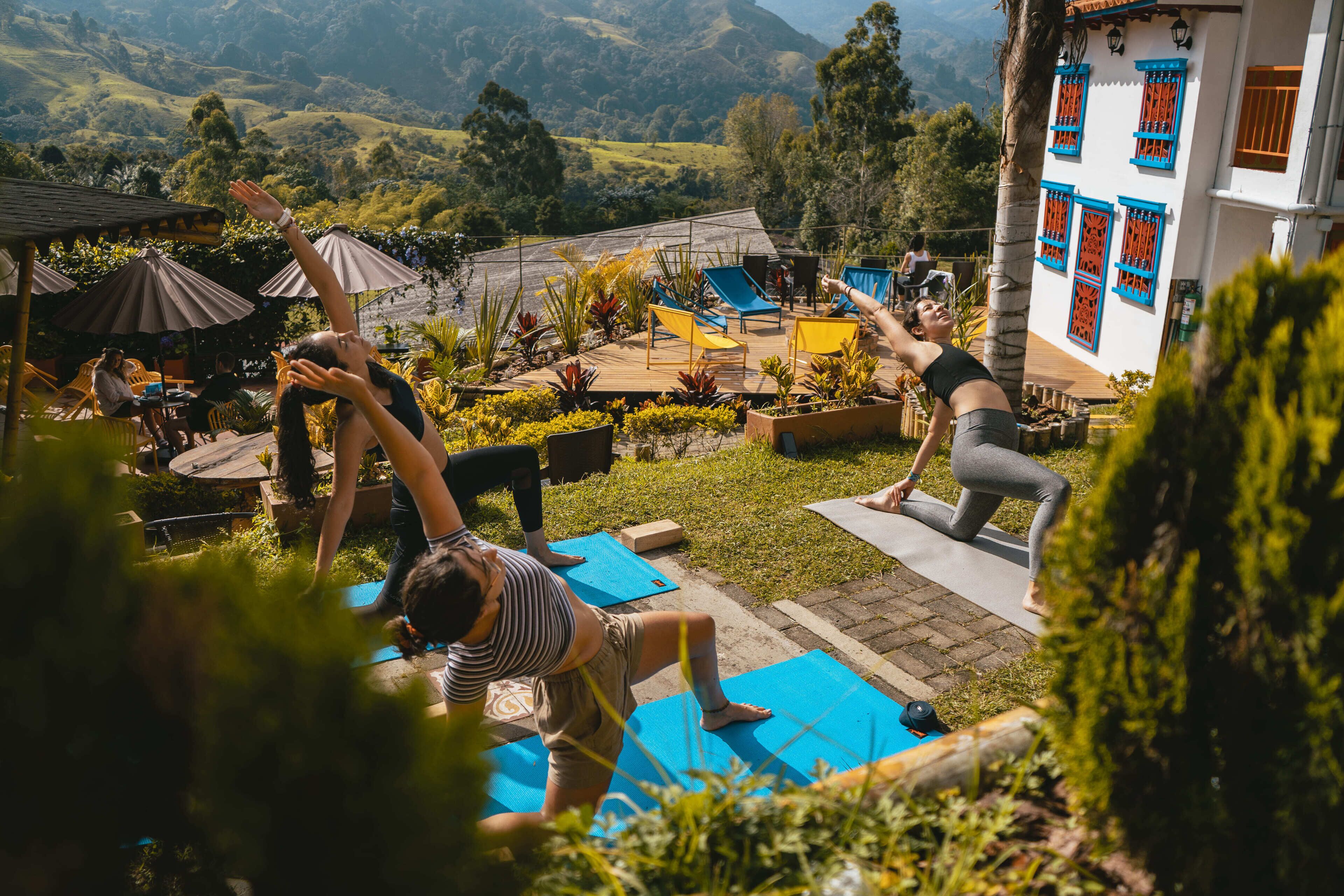 A yoga class in an outdoor setting with participants on mats, surrounded by greenery and a view of hills.