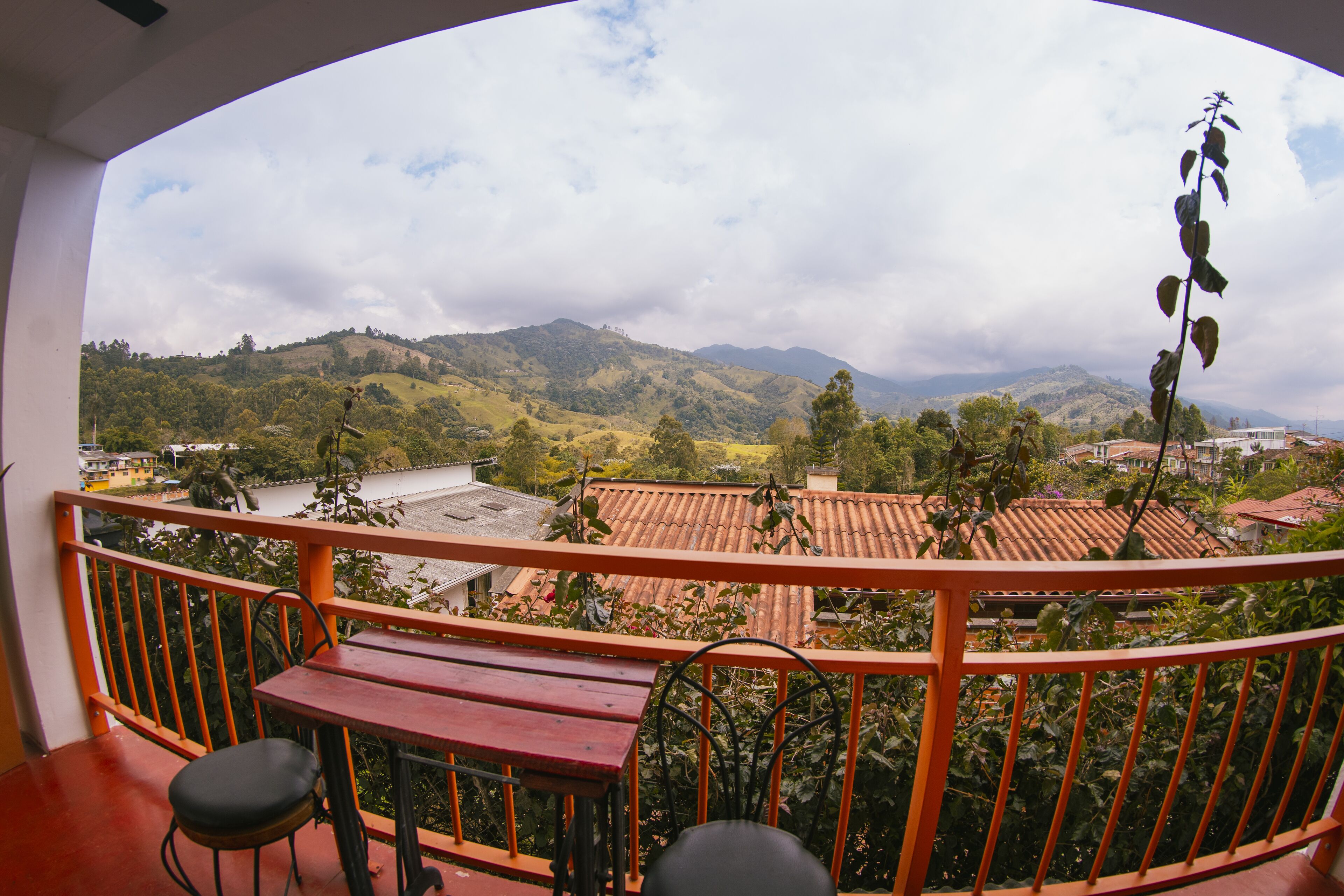 Un balcon donnant sur un paysage vallonné, une table en bois et deux chaises.