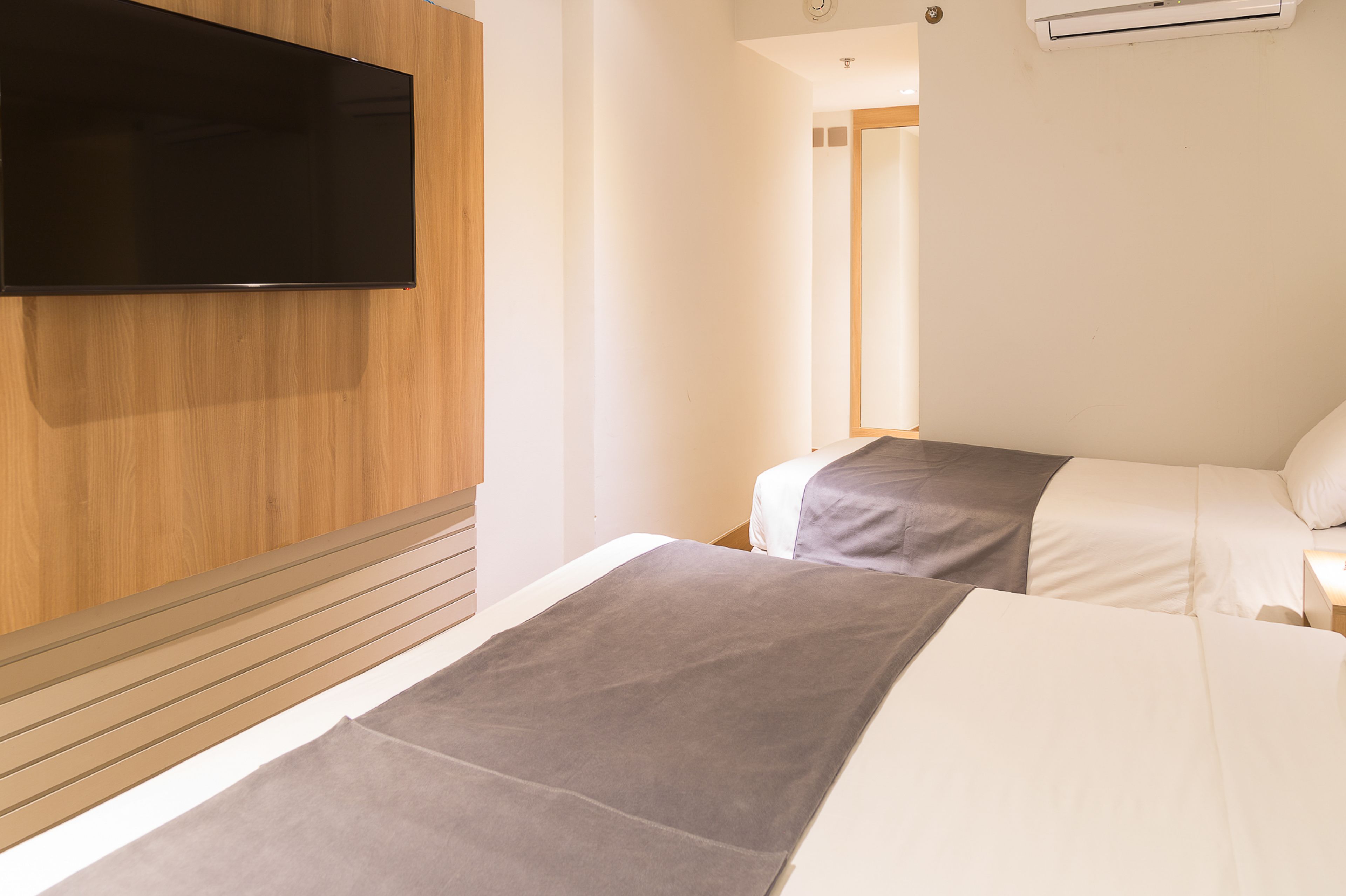 A hotel room with two beds, a flat-screen TV mounted on the wall, and an air conditioning unit.