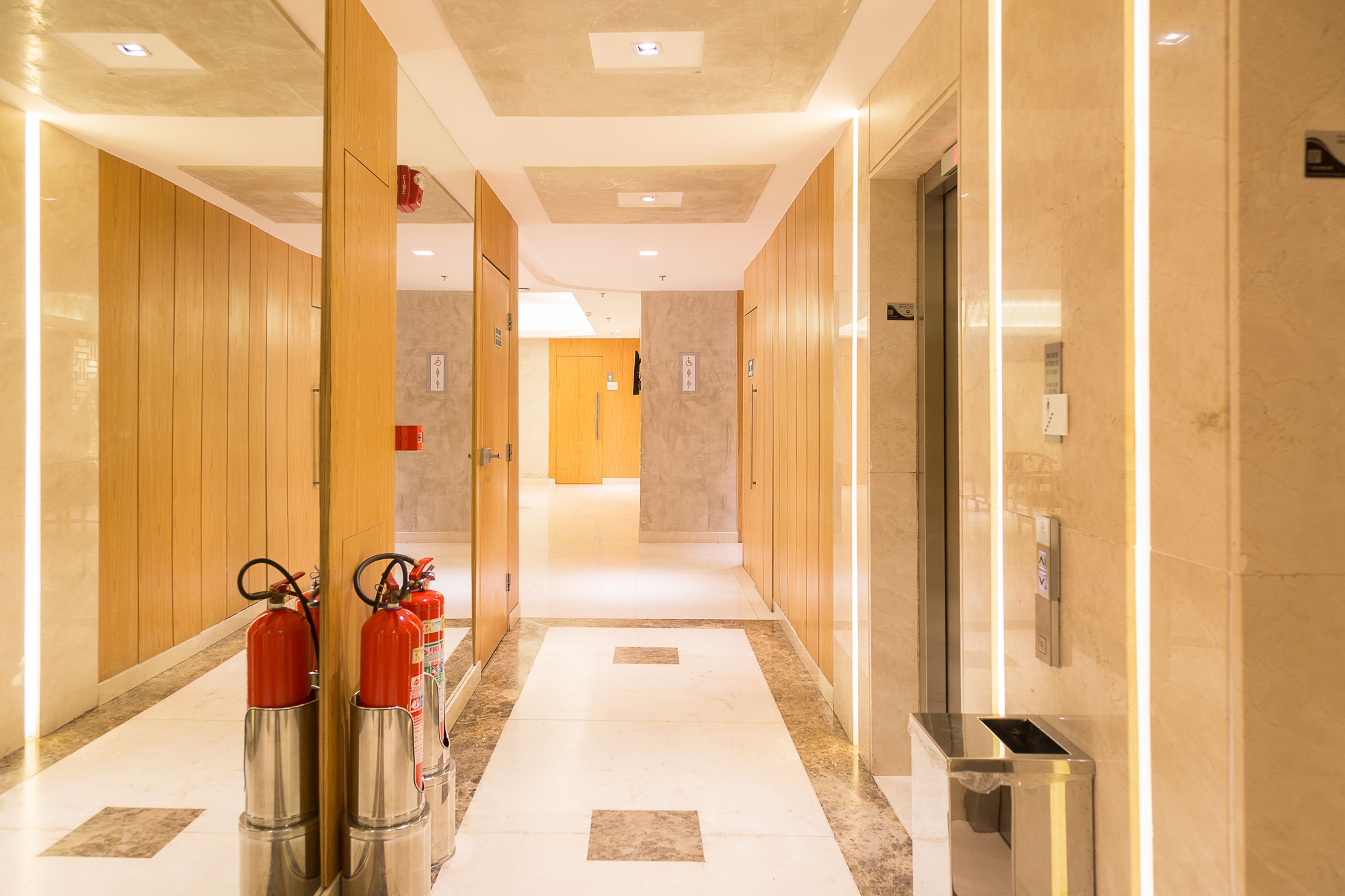 Een hotelgang met houten deuren, een brandblusser en een lift.