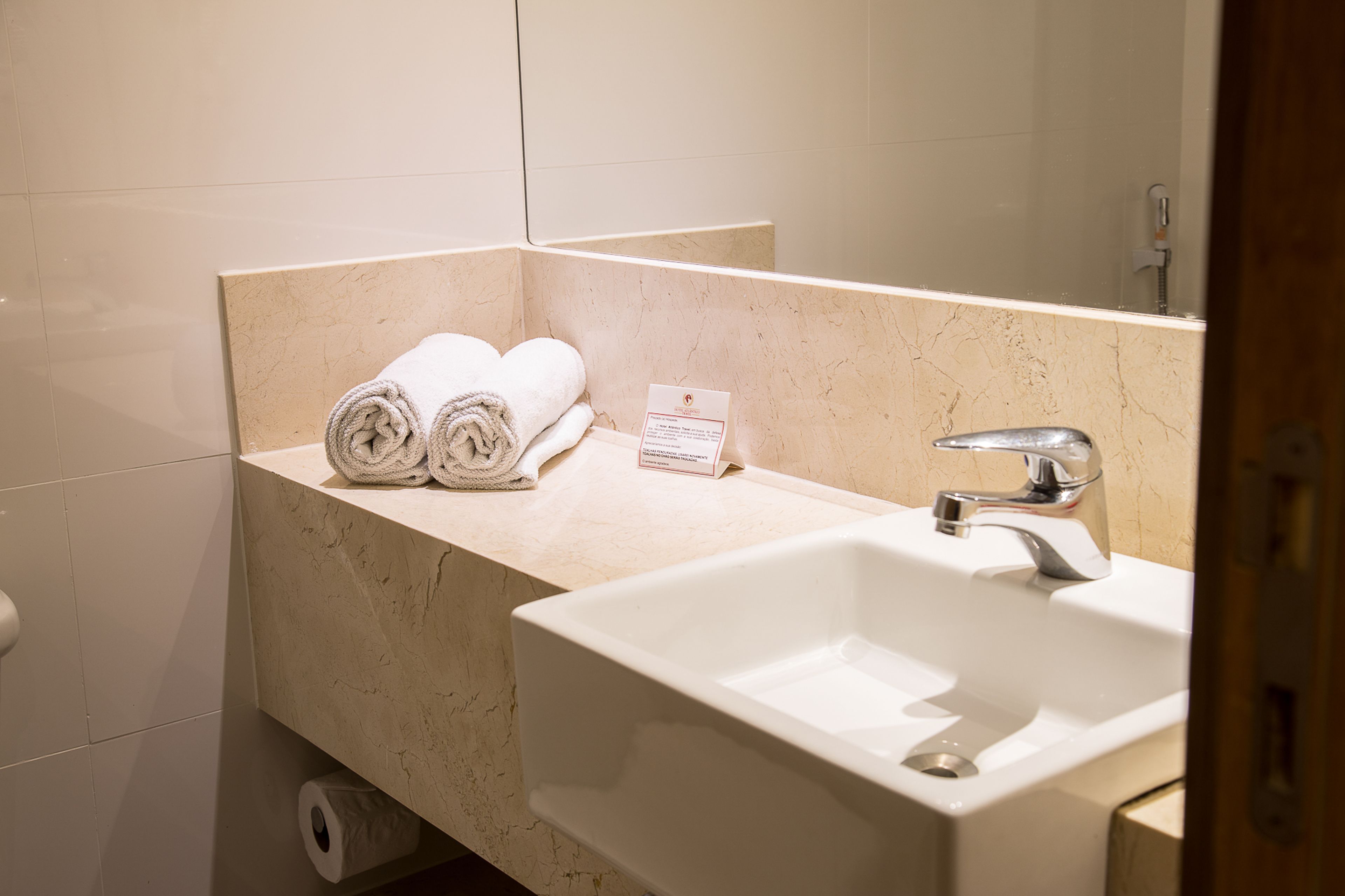 Une salle de bain avec un lavabo, un miroir et deux serviettes enroulées posées sur un comptoir.