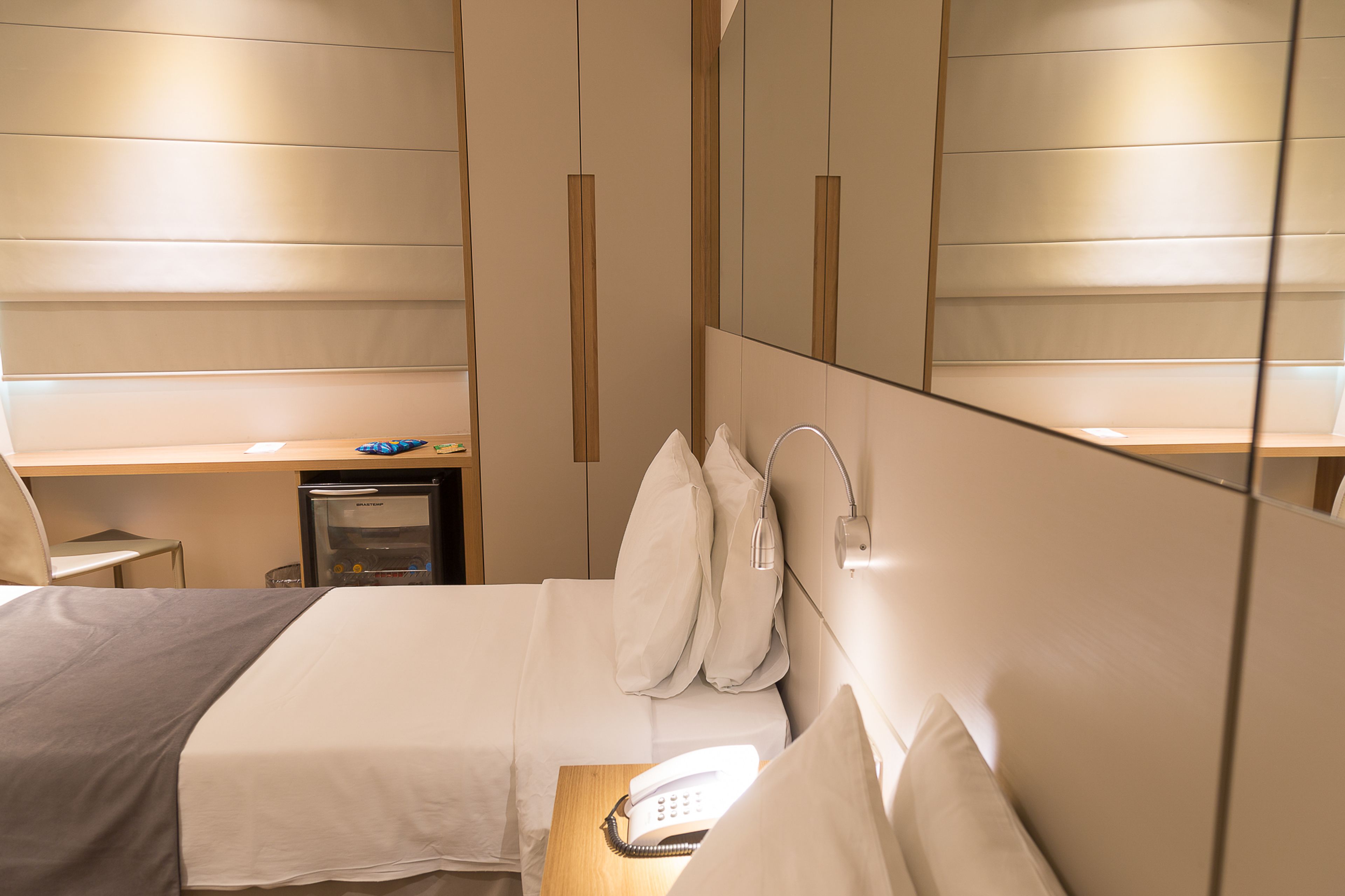 A hotel room with a bed, bedside table, and a desk with a chair.