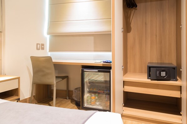 A compact hotel room with a bed, a desk with a chair, a minibar, and a wardrobe.