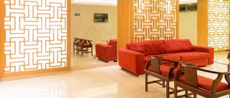 A modern lobby with a geometric patterned partition, a red sofa, wooden chairs, and a glass table.