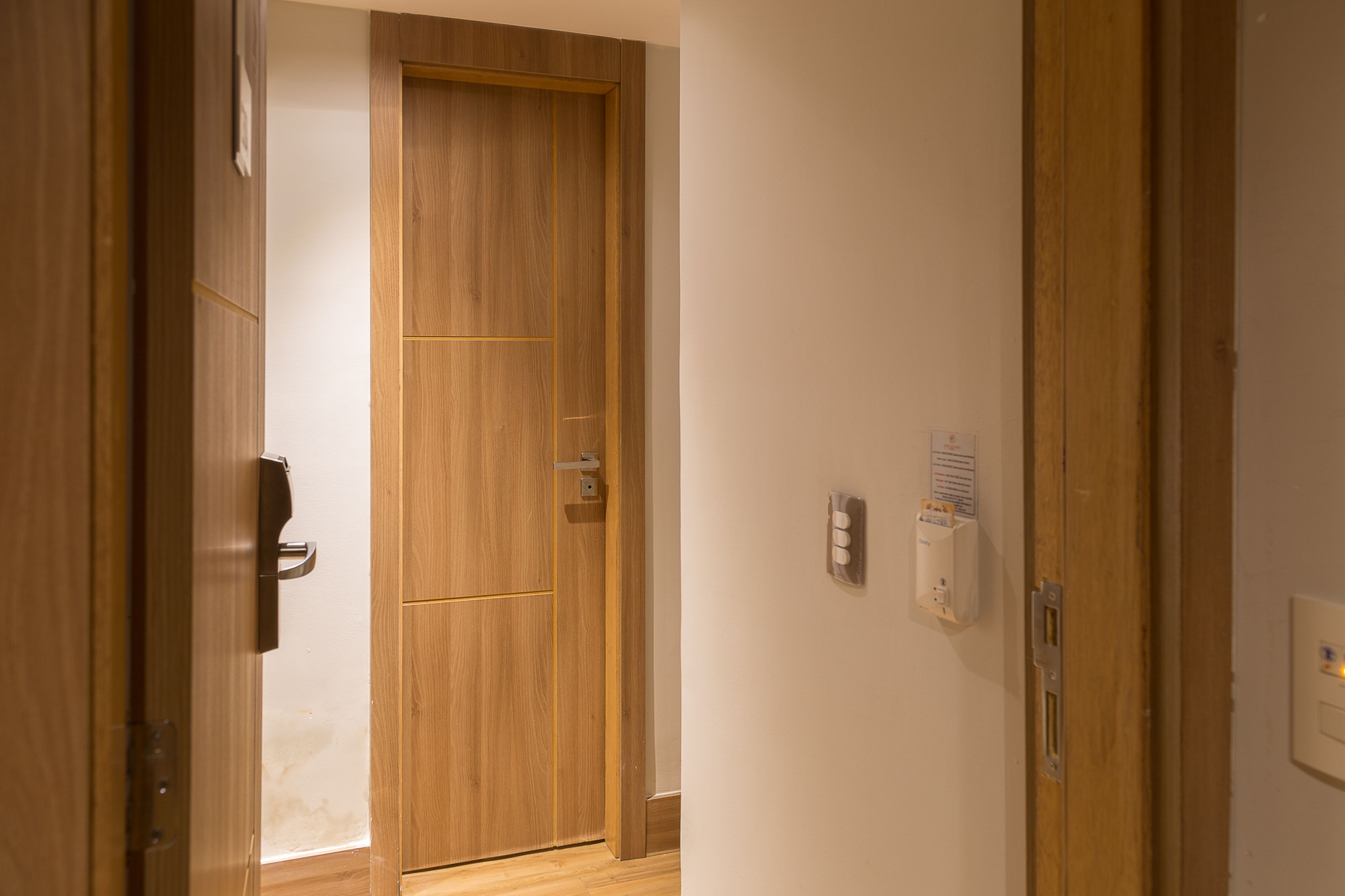 Un couloir avec des portes en bois et un interphone fixé au mur.