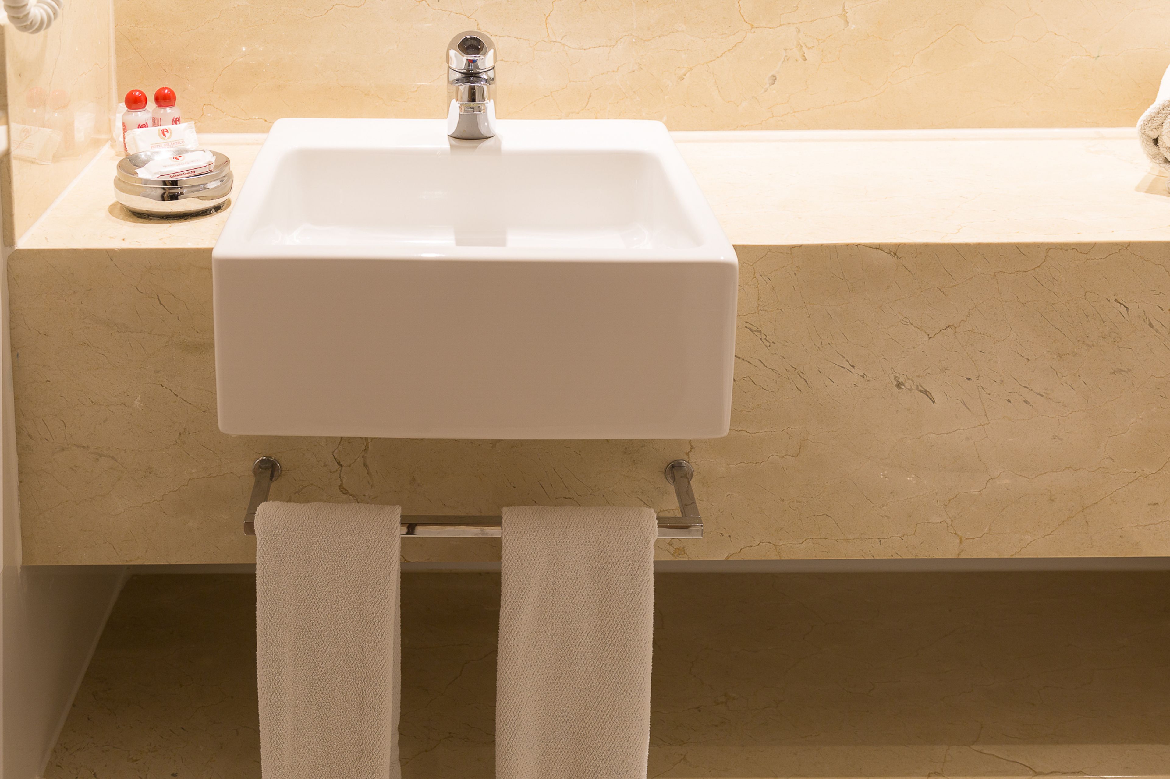 A bathroom with a white sink, a towel rack, and toiletries on the countertop.