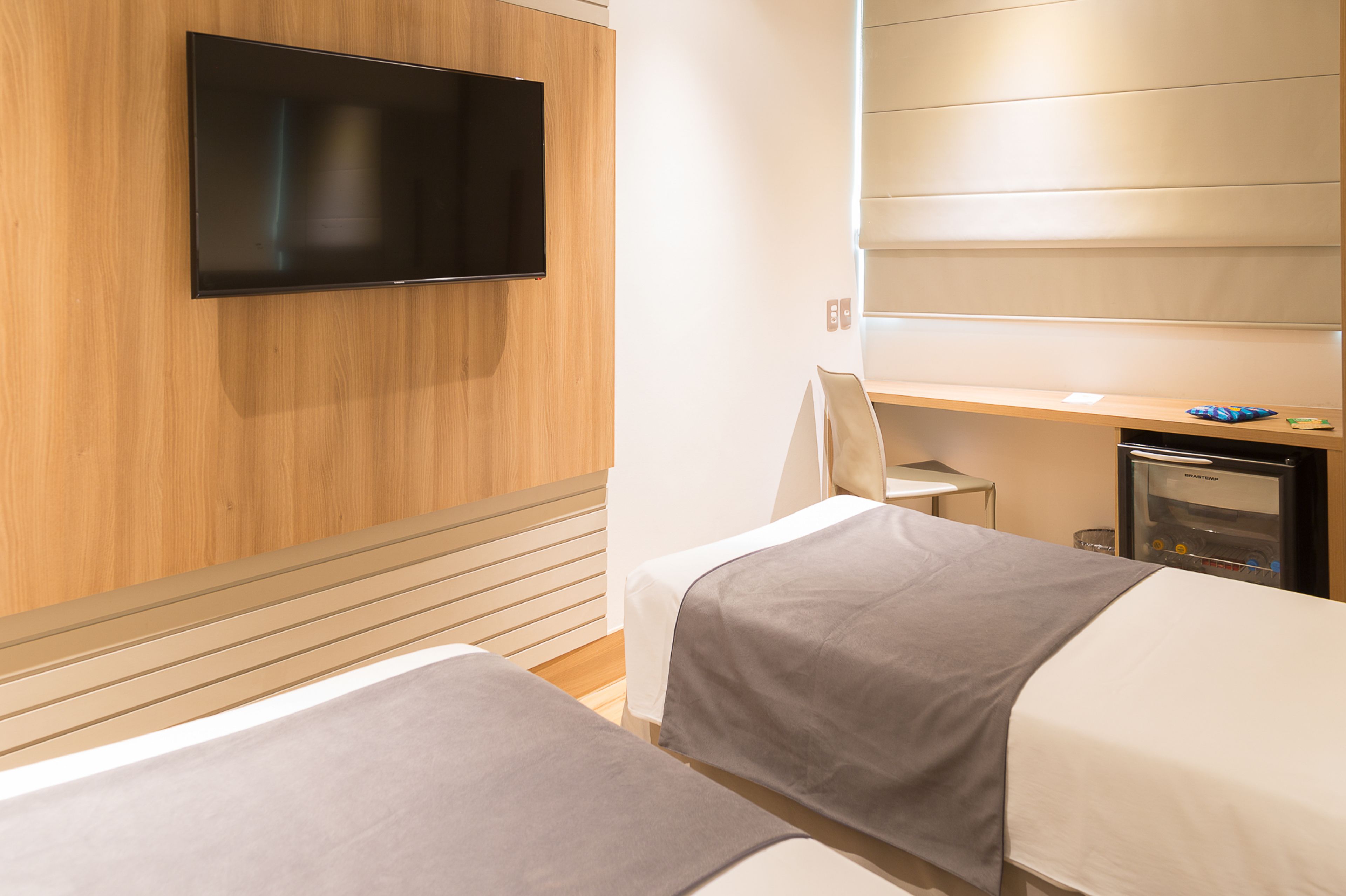A hotel room with two beds, a TV mounted on the wall, a small desk, and a minibar.