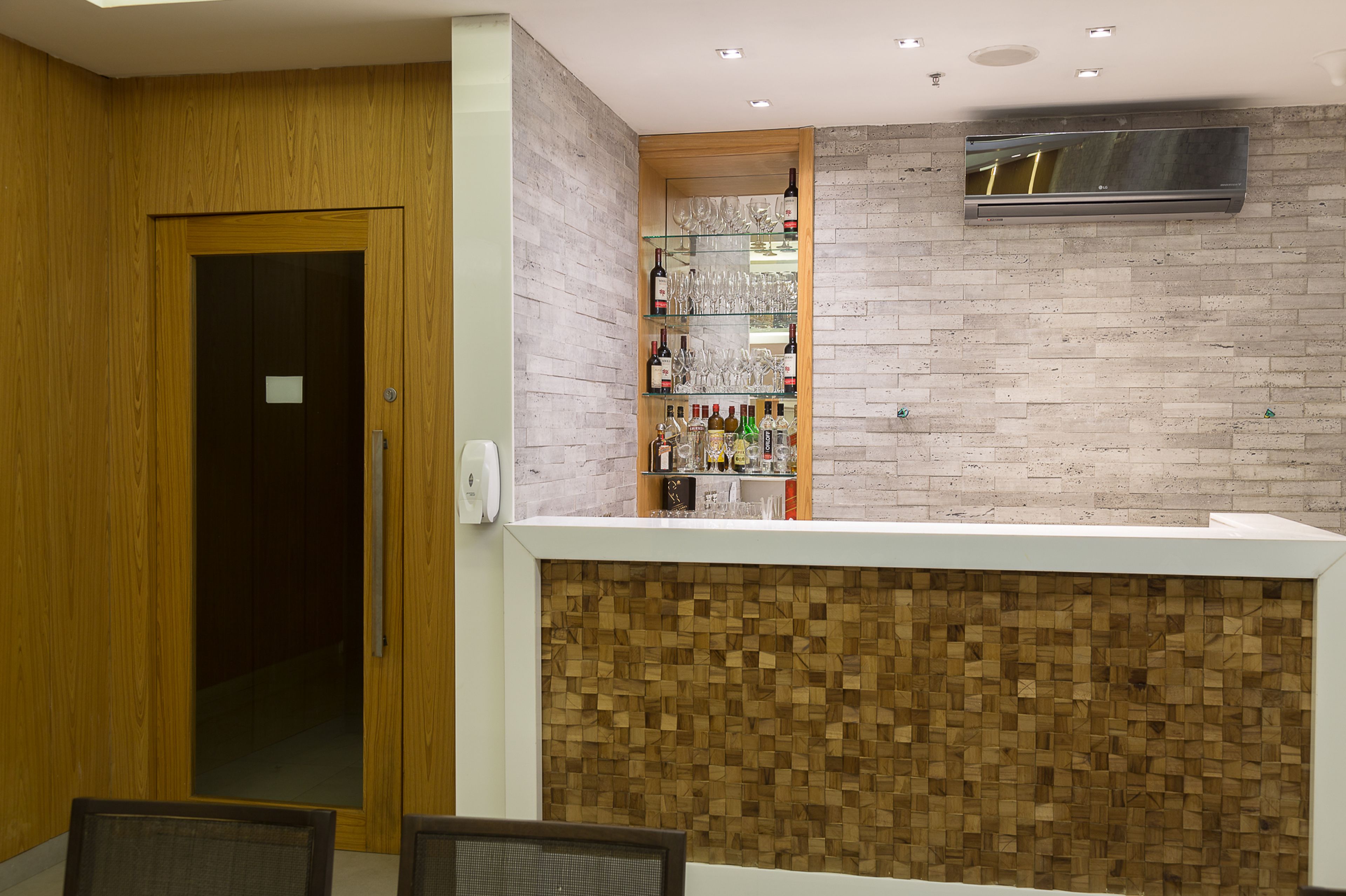 A reception area with a wooden door, a glass display case with wine bottles and glasses, and a brick wall.