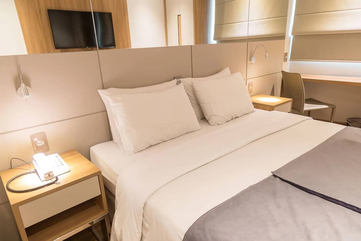 Una habitación de hotel moderna con cama, mesitas de noche, televisor y zona de ducha.