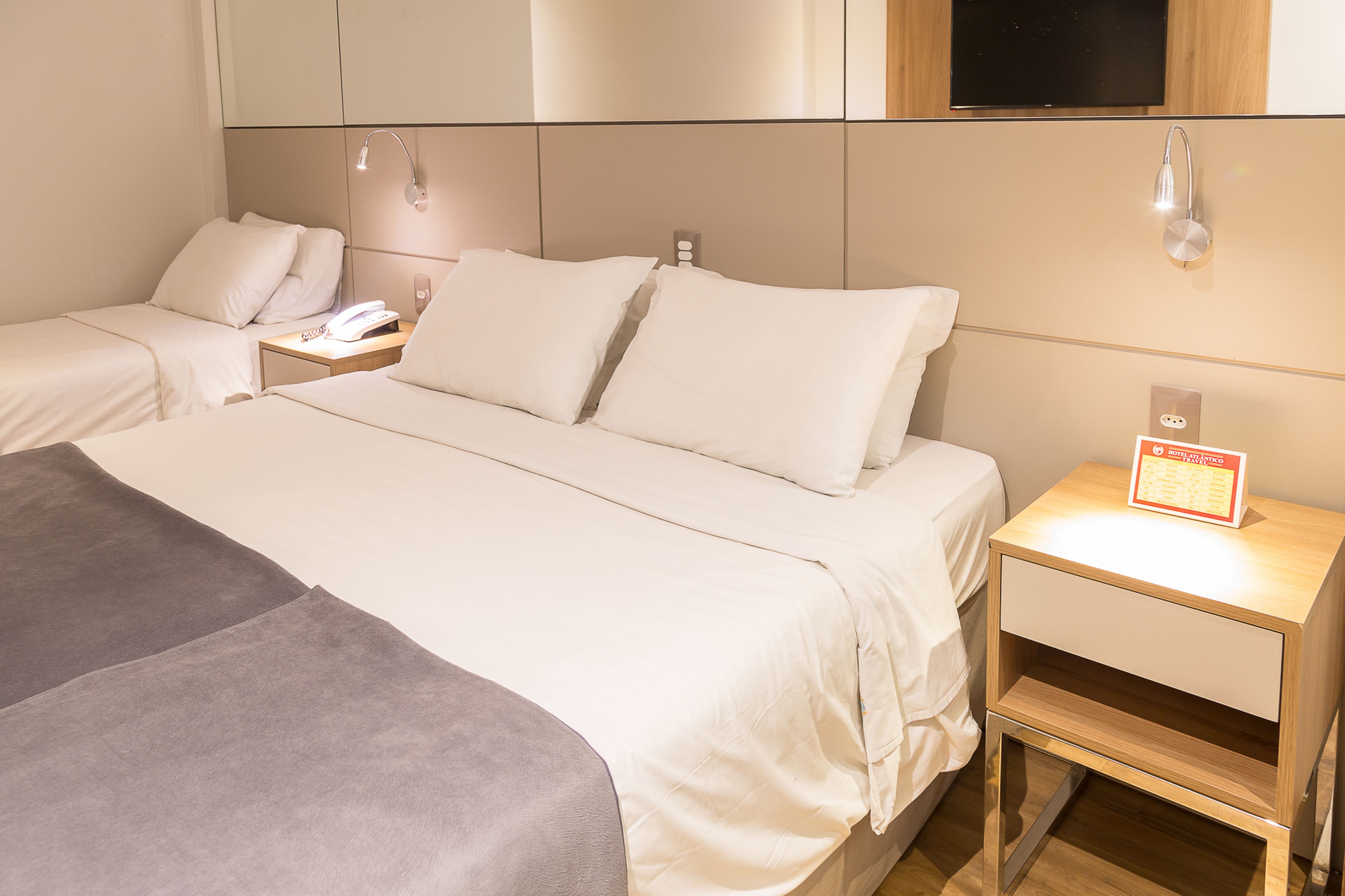 Une chambre d’hôtel avec deux lits, une table de chevet avec une lampe et une petite table d’appoint avec un panneau.