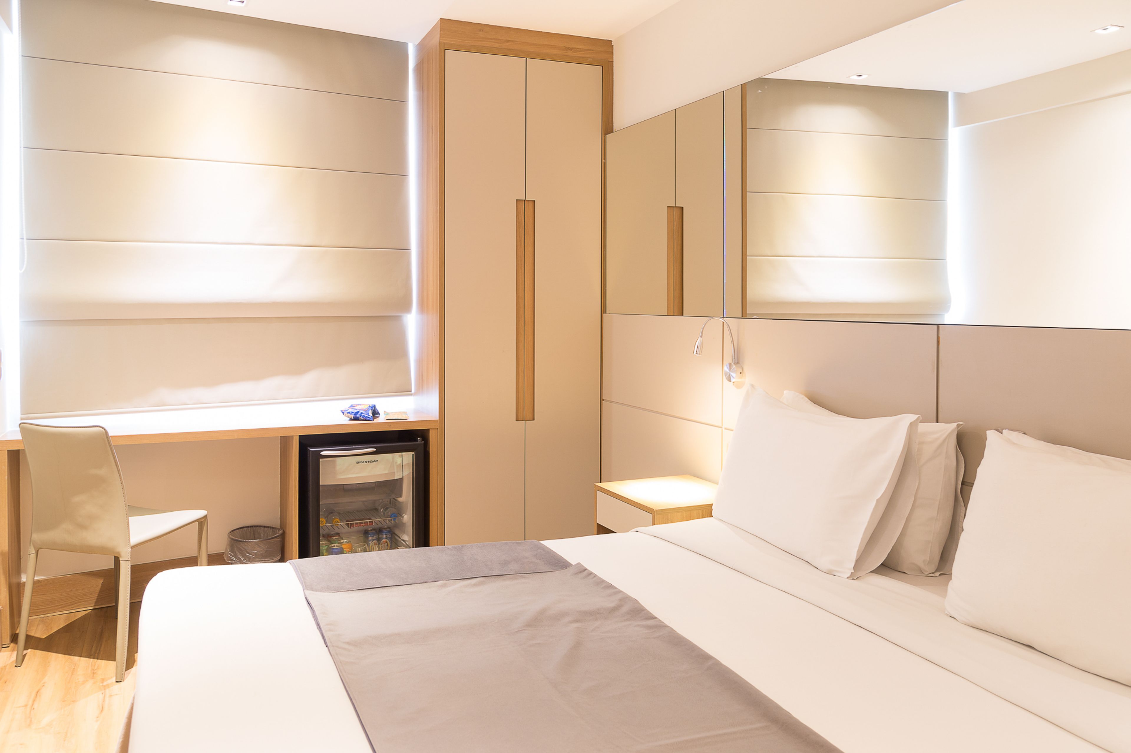 A modern hotel room with a bed, a desk, and a refrigerator.