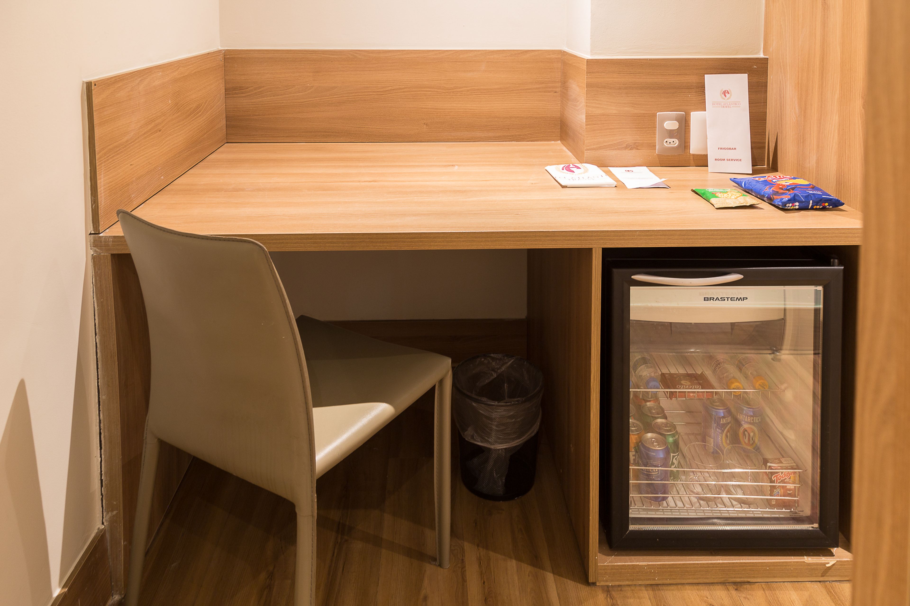 Ein Schreibtisch im Eckbereich mit Stuhl, Mülleimer und einem Minikühlschrank, gefüllt mit Getränken.