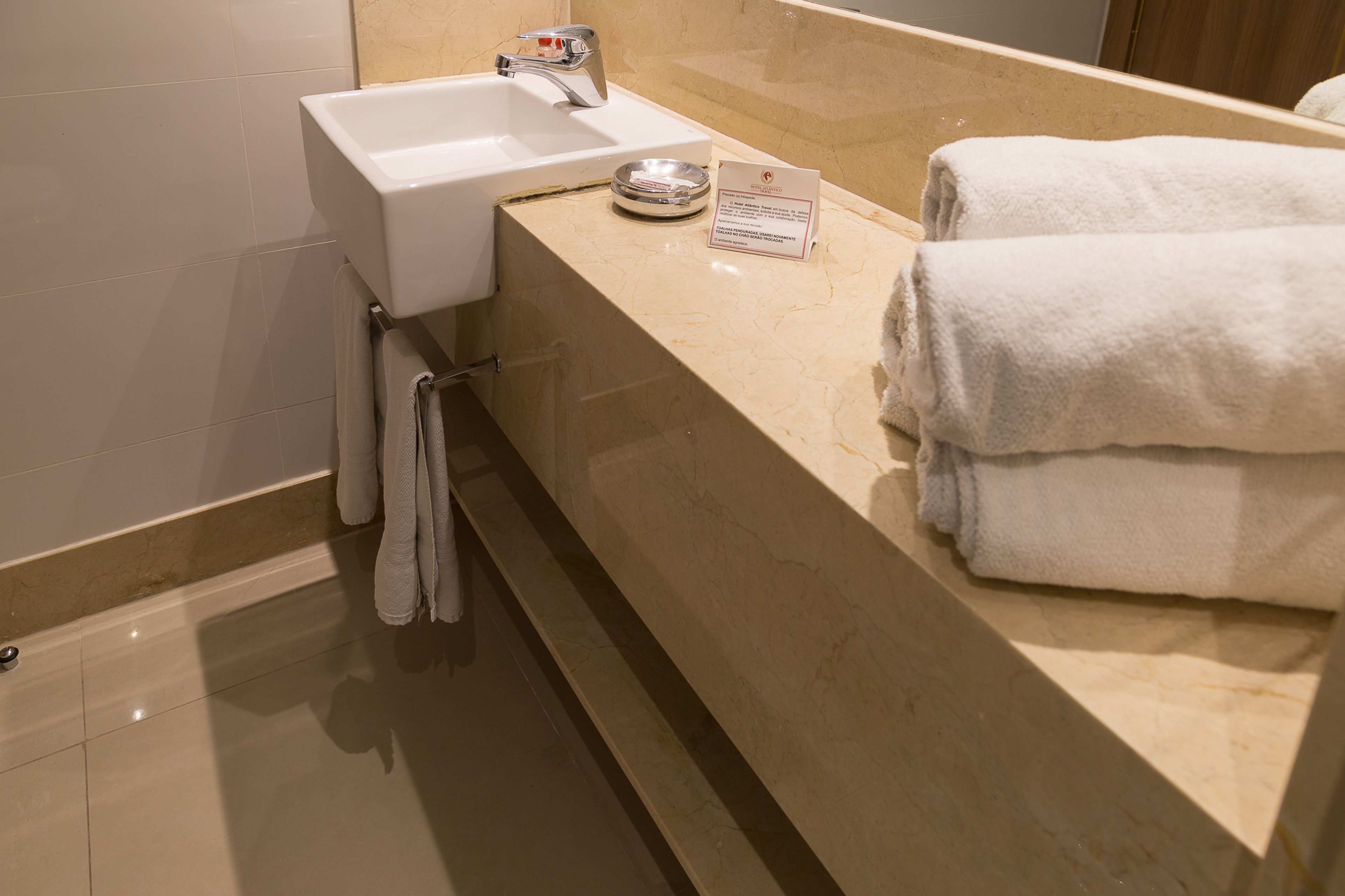 A bathroom with a sink, towel rack, and a sign on the counter.