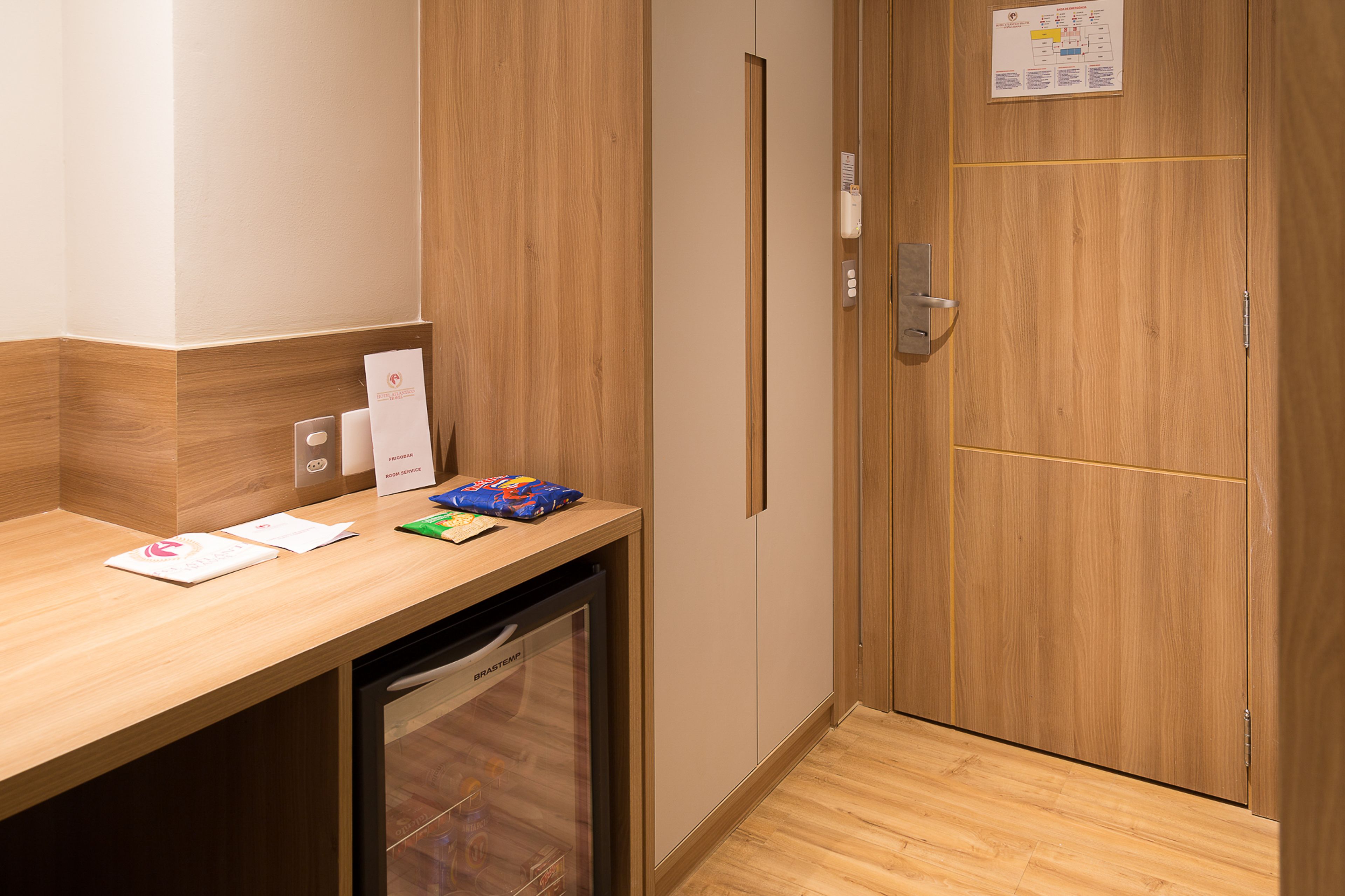 A hotel room with a wooden counter, a small refrigerator, and a wooden door with a lock.