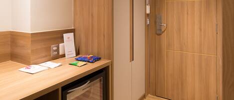 A hotel room with a wooden counter, a small refrigerator, and a wooden door with a lock.