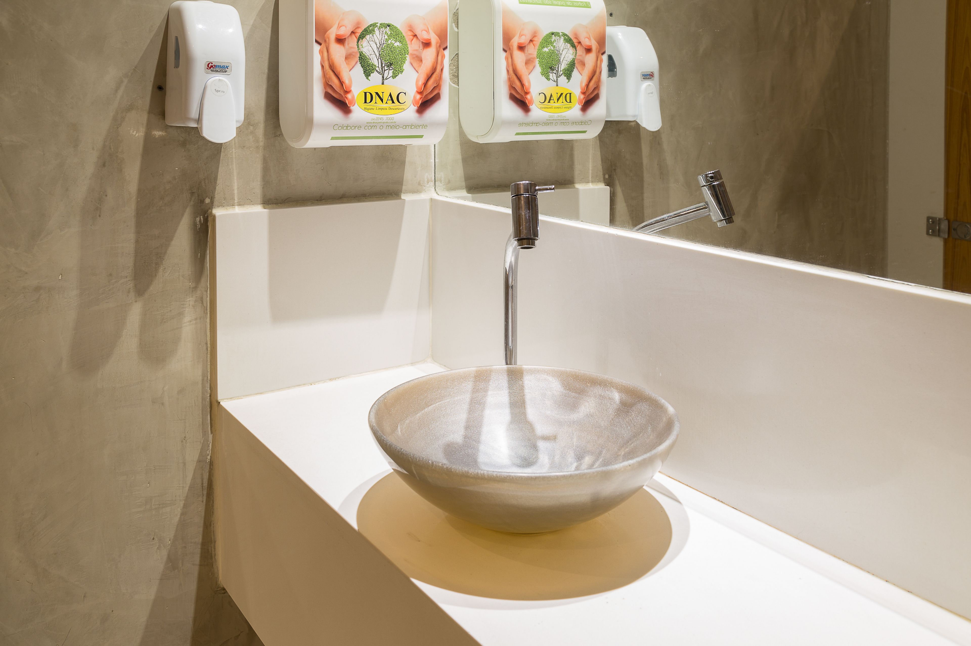 Een badkamer met een wit wastafel, een chromen kraan en twee zeepdispensers gelabeld DNAC.
