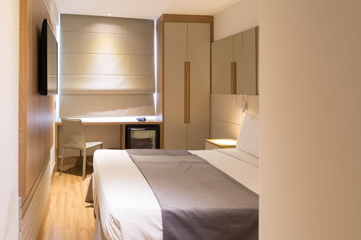 Habitación de hotel con cama, escritorio, silla, televisión y armario.