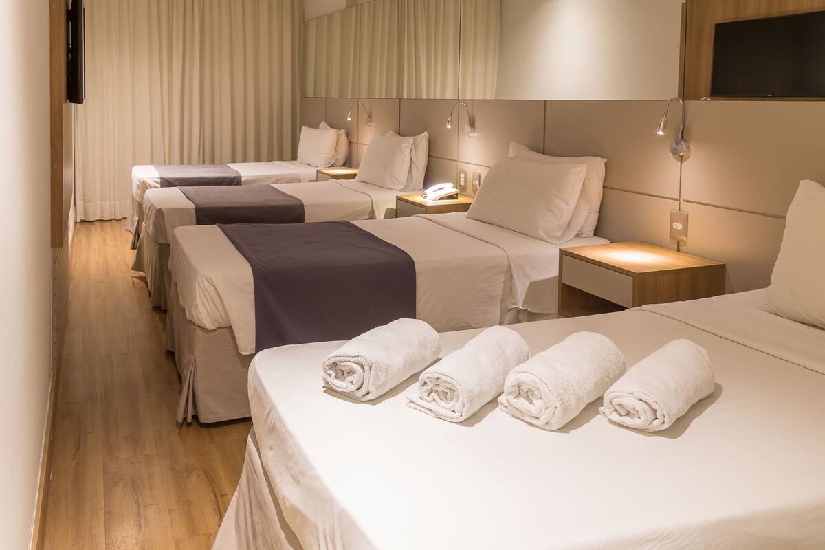Habitación de hotel con tres camas, cada una con mesita de noche, lámpara y teléfono.