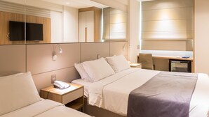 Una habitación de hotel con dos camas, televisión, escritorio y espejo.