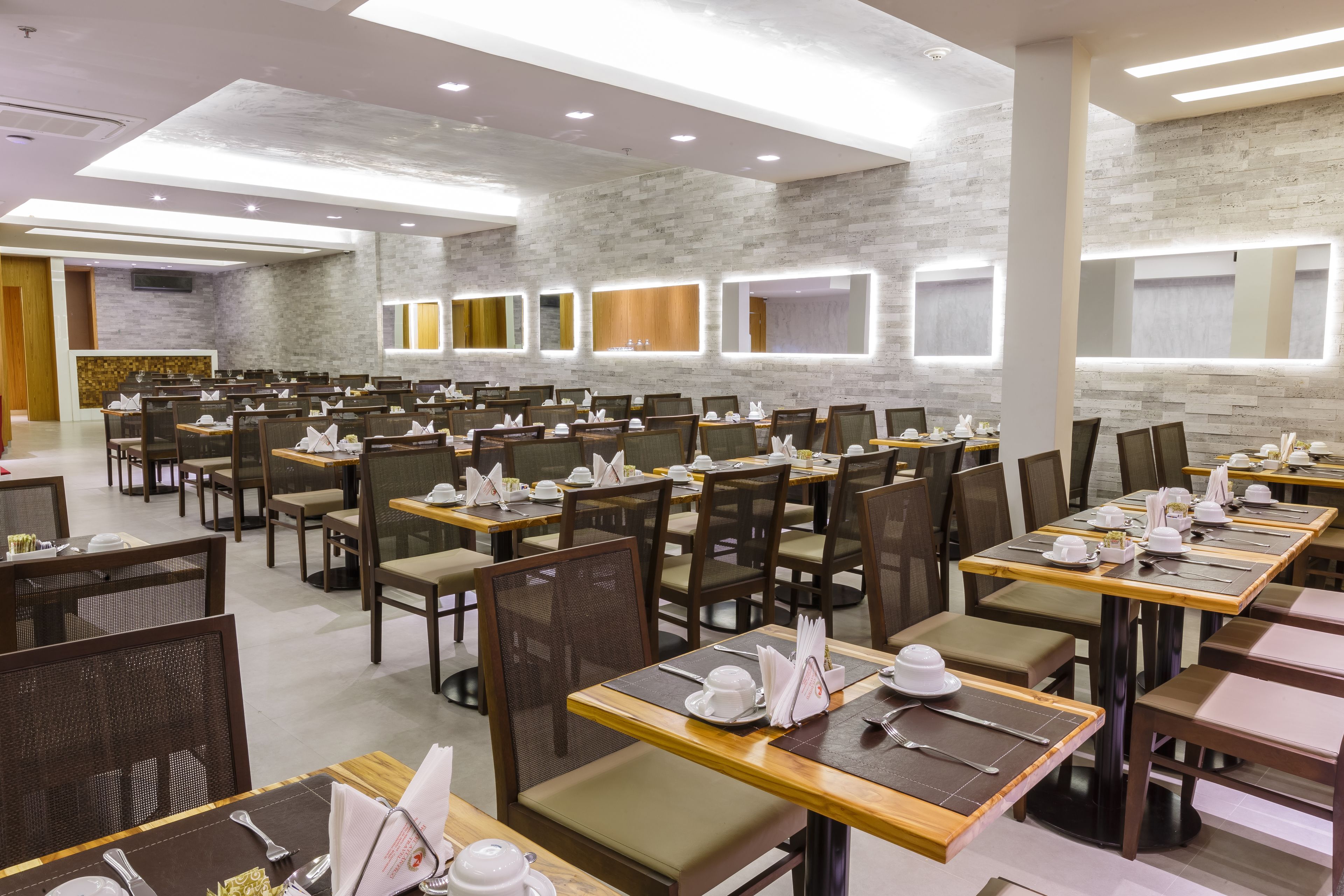 Un comedor amplio con varias mesas y sillas, cada conjunto con vajilla y servilletas blancas.