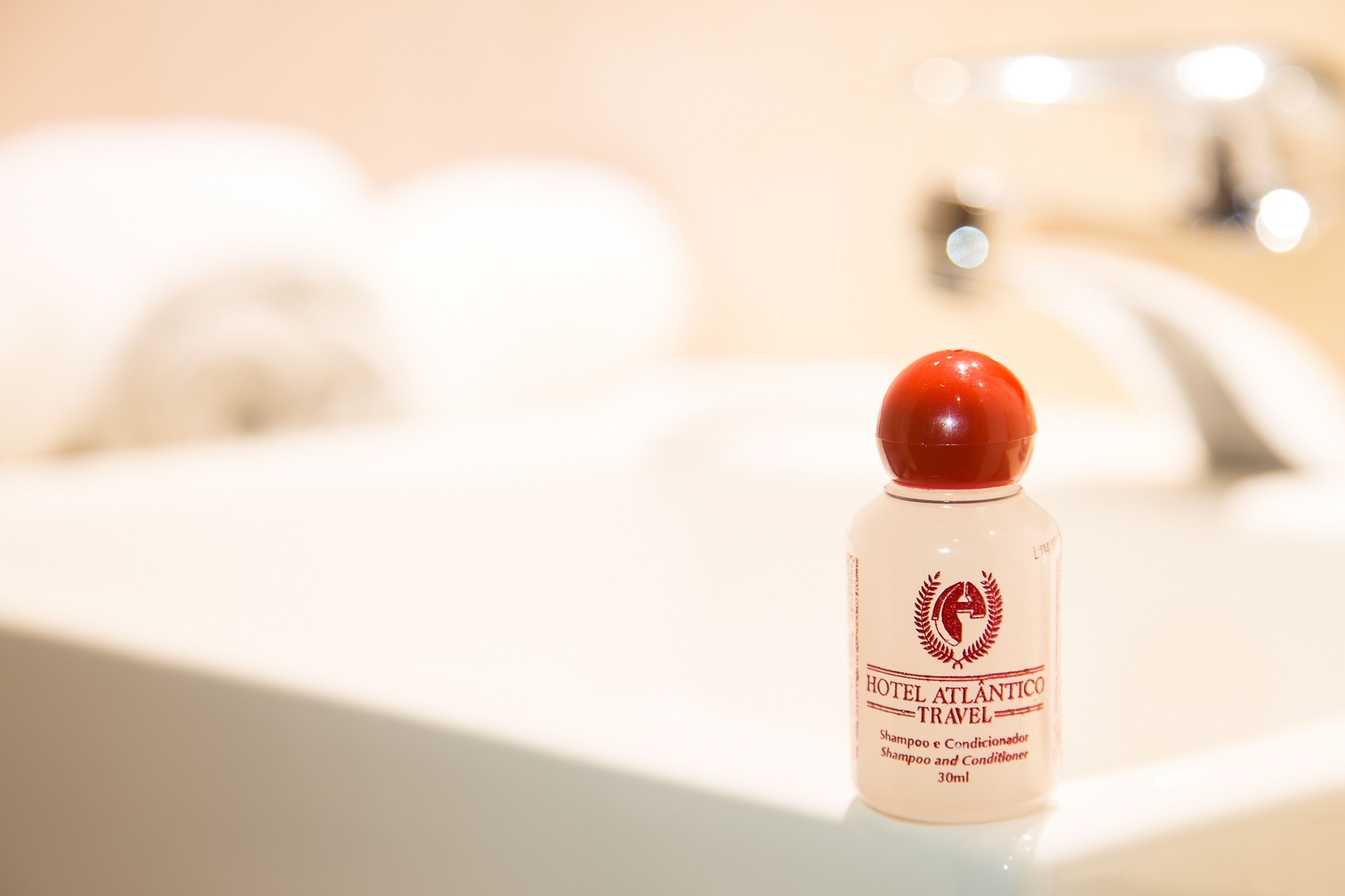 Una botella de champú y acondicionador Hotel Atlántico Travel sobre un lavamanos de baño.