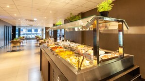 Zona de buffet con diversas opciones de comida, un área de estar con mesas y sillas, y vistas al exterior a través de amplios ventanales.