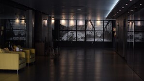 Un moderno hall con una amplia ventana que ofrece vistas a un puente y un río, asientos amarillos y un interior limpio y oscuro.