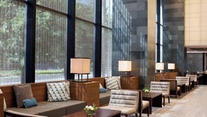 Un moderno vestíbulo de hotel con una larga recepción, zona de estar con sofás y sillones, y ventanas amplias que ofrecen vistas a zonas verdes.