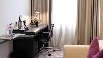 A hotel room with a desk, chair, and a sofa.