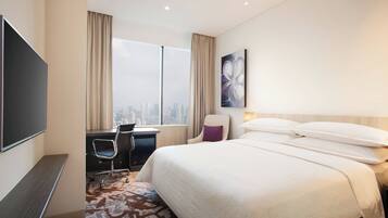 Habitación de hotel con una cama grande, un escritorio con silla, televisión y vista a la ciudad.