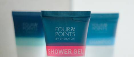 Three shower gel containers on a glass shelf.