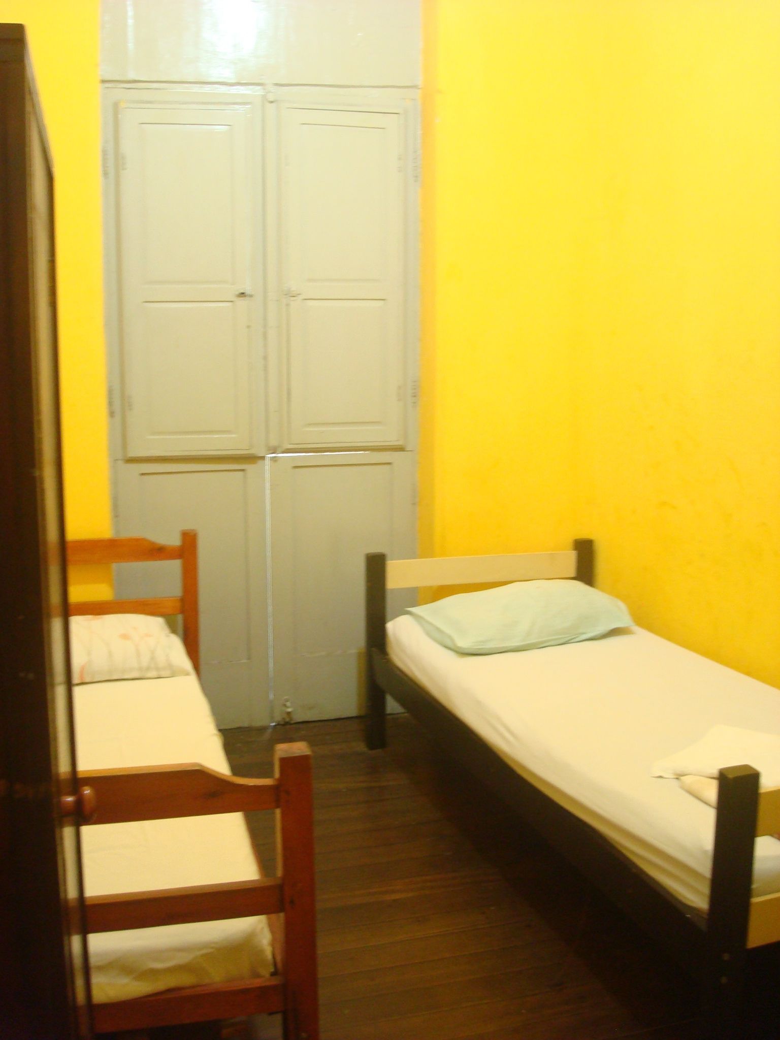 A small, narrow room with two wooden beds and a wardrobe.